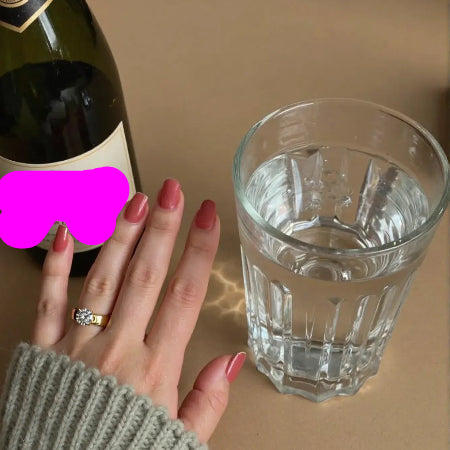 Stainless steel zircon ring on woman's hand, stylish jewelry displayed beside glass of water and wine bottle.