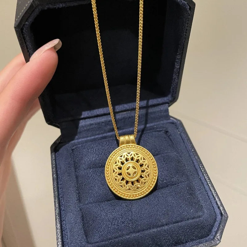 Close-up of a gold vintage round pendant necklace with intricate floral patterns, displayed in a dark blue jewelry box
